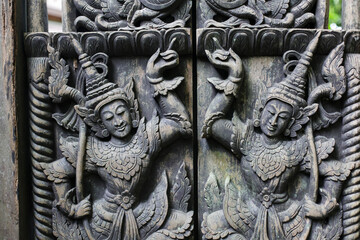 A carved wooden door with Thai deity motifs is commonly found in Thai temples.