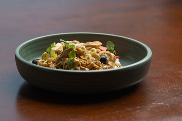 A vibrant meal featuring noodles, vegetables, and garnishes is elegantly presented in a dark bowl on a polished wooden surface.