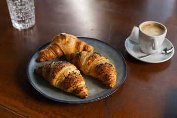A brunch plate holds freshly baked croissants alongside a small cup of coffee on a wooden table in a warm, inviting cafe.