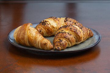 Three golden croissants sit on a ceramic plate, showcasing flaky layers and a tempting texture, perfect for breakfast or a snack.