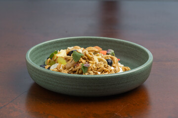 A colorful bowl of granola topped with fresh fruits and nuts sits on a wooden table, showcasing a...