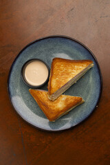 Warm golden grilled cheese sandwich cut into triangles sits on a blue plate next to a small bowl of creamy dipping sauce.