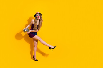 Stylish young woman in colorful outfit holding a disco ball, striking a playful pose on a vibrant...