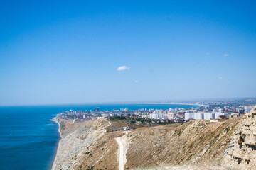 A stunning panoramic view of the seascape of the Black Sea, the Anapa Bay, the foot of the Caucasus Mountains and the tourist city of Anapa from a steep rocky cliff of a white limestone bald mountain.