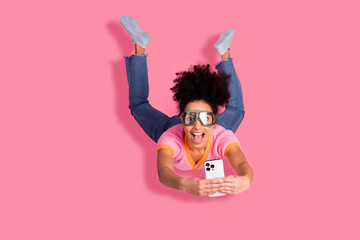 Young woman with afro haircut enjoying playfully holding smartphone on vibrant pink background,...