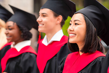 Multiracial group of cheerfully graduates having graduation ceremony, wearing black and red...