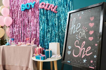Decorated gender reveal party scene featuring table with sweets, balloons, wrapped gifts, metallic...