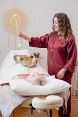 Woman performing sound healing therapy with Tibetan singing bowls placed on a client's body. The...