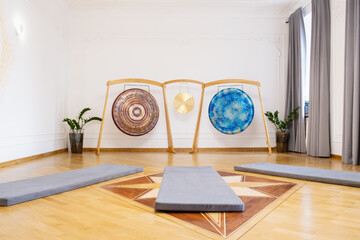 Peaceful meditation room showcasing three gongs mounted on wooden stands, surrounded by soft gray...