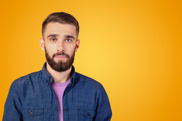 Portrait of charismatic bearded young man in casual clothes looking at camera over orange studio background. Serious millennial guy with attractive face posing, feeling calm and peaceful