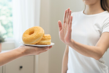 Diet concept, asian young woman hand push out, deny sugar donut, doughnut and sweet taste food on plate, fighting to keep it from getting fat when person bring to me. Healthy nutrition of weight loss.