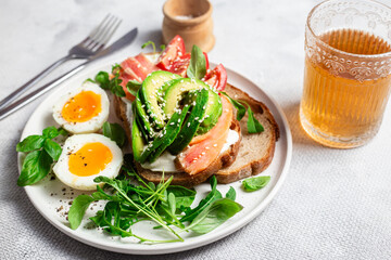  Sandwich with salmon, avocado, tomatoes and egg in a white plate on the table close-up. Healthy breakfast