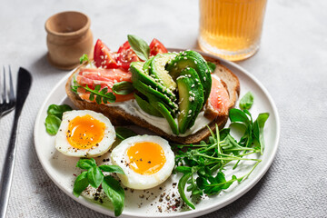  Sandwich with salmon, avocado, tomatoes and egg in a white plate on the table close-up. Healthy breakfast
