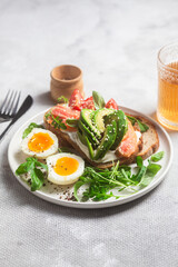  Sandwich with salmon, avocado, tomatoes and egg in a white plate on the table close-up. Healthy breakfast