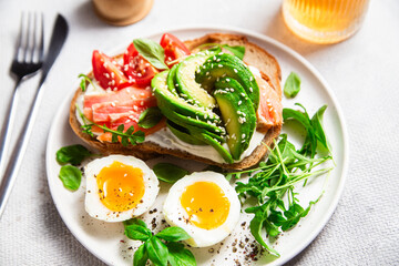  Sandwich with salmon, avocado, tomatoes and egg in a white plate on the table close-up. Healthy breakfast