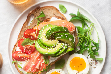  Sandwich with salmon, avocado, tomatoes and egg in a white plate on the table close-up. Healthy breakfast