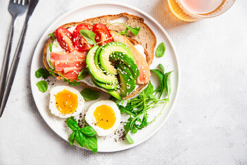  Sandwich with salmon, avocado, tomatoes and egg in a white plate on the table close-up. Healthy breakfast