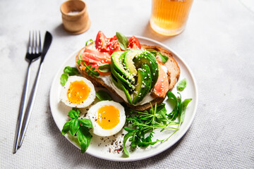  Sandwich with salmon, avocado, tomatoes and egg in a white plate on the table close-up. Healthy breakfast