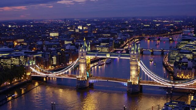 London's Iconic Twilight: An aerial view of London's Tower Bridge at dusk. Illuminated against the twilight sky, the bridge shines, reflecting in the calm water of the river.