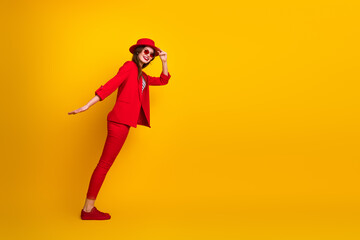 Young stylish woman in a red suit posing on a vibrant yellow background expressing joy and trendy modern fashion