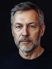 Portrait middle-aged man grey hair beard looking directly at camera dark background, serious gaze