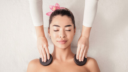 Beautiful young asian woman relaxing in spa salon, getting hot stone massage treatment, korean...