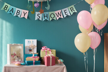 Table decorated for gender reveal party featuring wrapped gifts, cupcakes, pastel balloons and baby...