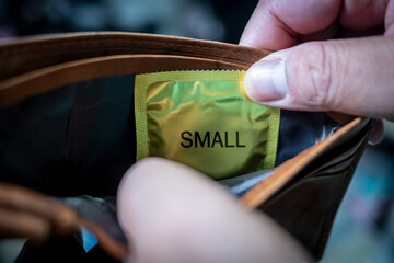 A man's hand is taking out a small-sized condom from his wallet. Small penis syndrome problem
