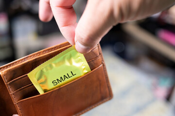 A man's hand is taking out a small-sized condom from his wallet. Small penis syndrome problem
