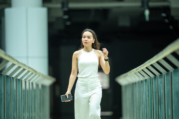 A woman is walking down a bridge with a cell phone in her hand