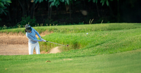 A woman is swinging a golf club at a ball