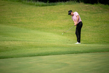 A man in a pink shirt is playing golf