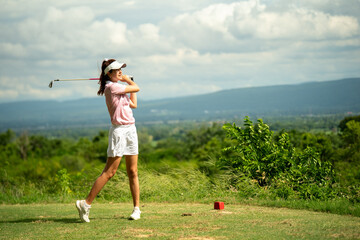 A woman is swinging a golf club on a grassy field