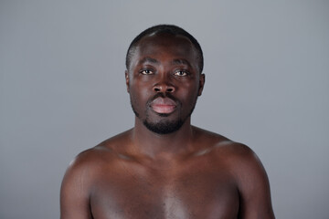 Portrait of shirtless African American man with short hair and beard, looking straight ahead in...