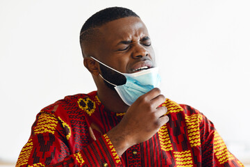 Young African Man Taking Off Medical Mask At Work, Can Not Breathe, Black Guy In Traditional...