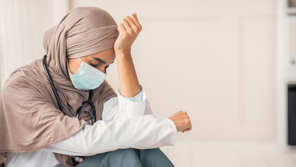 Sad arab woman doctor having difficult day at clinic, wearing protective face mask, sitting next to...