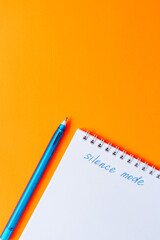 Notebook with the phrase silence mode and a blue pen on bright orange background. Pop art school or office stationery concept. High quality photo