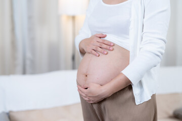 Close up of Asian pregnant woman's bare belly with hands gently resting expressing love care and emotional bonding between mother and unborn baby in intimate peaceful moment before childbirth