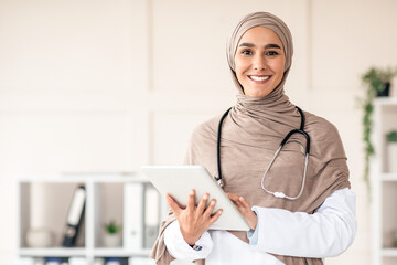 Modern technologies in healthcare concept. Happy female doctor in hijab with digital tablet posing...