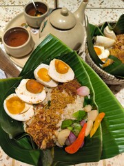 An enticing plate of traditional Indonesian Nasi Bakul Telur Asin, beautifully presented on a banana leaf with savory salted eggs and flavorful accompaniments