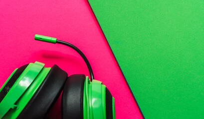 Close-up of green headphones with mic on pink and green paper backdrop. Trendy flat lay for digital lifestyle, gaming, and youth culture content. High quality photo