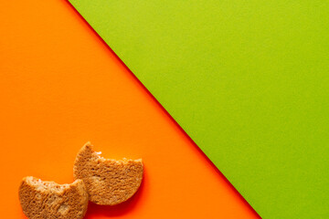 Two bitten cookies on bright orange and green paper background. Minimalist geometric food composition in vibrant pop art style. High quality photo