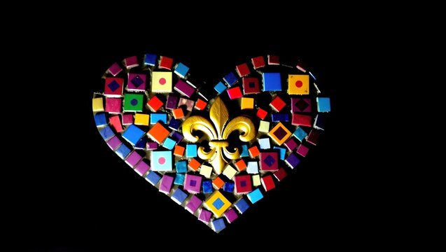 A heart-shaped mosaic made of colorful tiles featuring a golden fleur-de-lis at the center. Ornate and vibrant against a dark background.