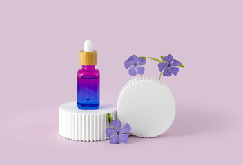 bottle of essential oil with a pipette and periwinkle flowers on a white podium on a purple...