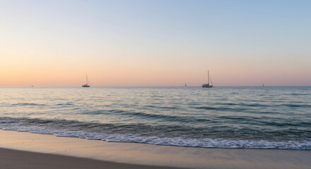 Sailboats glide across the ocean at sunset near the sandy beach