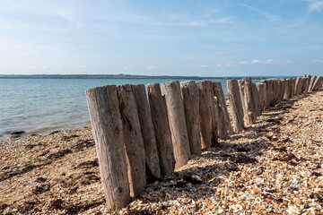 old wooden groynes on the beach with shadows cast by sunshine and the sea in the background
