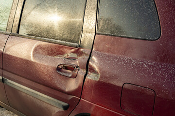 The door and rear wing of a red car are dented after an accident. Minor damage after an accident. Early spring morning