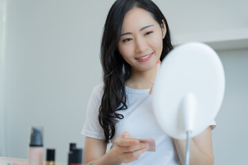 Beautiful Asian woman sit in front of a mirror. face of a healthy woman applying cream and makeup....
