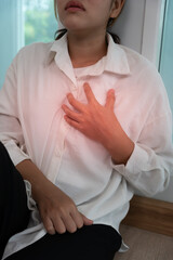 hand hold chest with heart attack symptoms, asian woman have chest pain caused by heart disease, leak, dilatation, enlarged coronary heart, press on the chest with a painful expressio