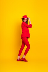Stylish young woman in red outfit with trendy accessories standing confidently against vibrant yellow studio background